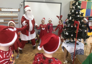 dzieci tańczą w kole z Mikołajem wokół choinki i śpiewają